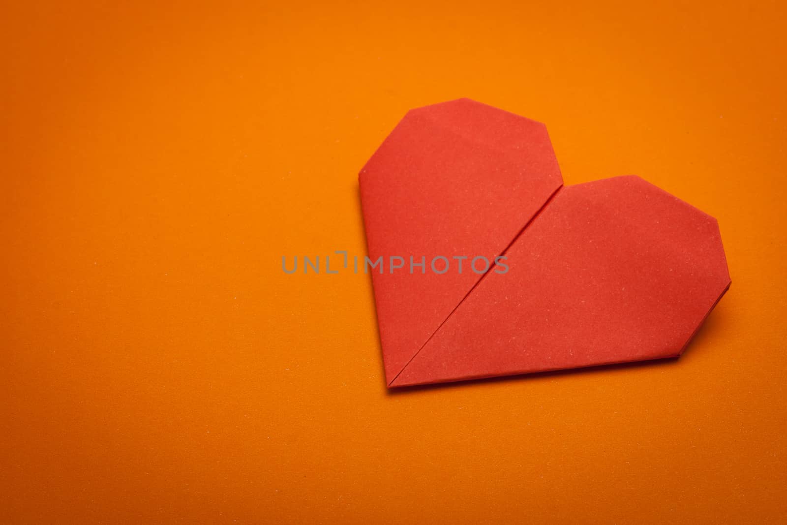 red origami paper heart on orange paper background