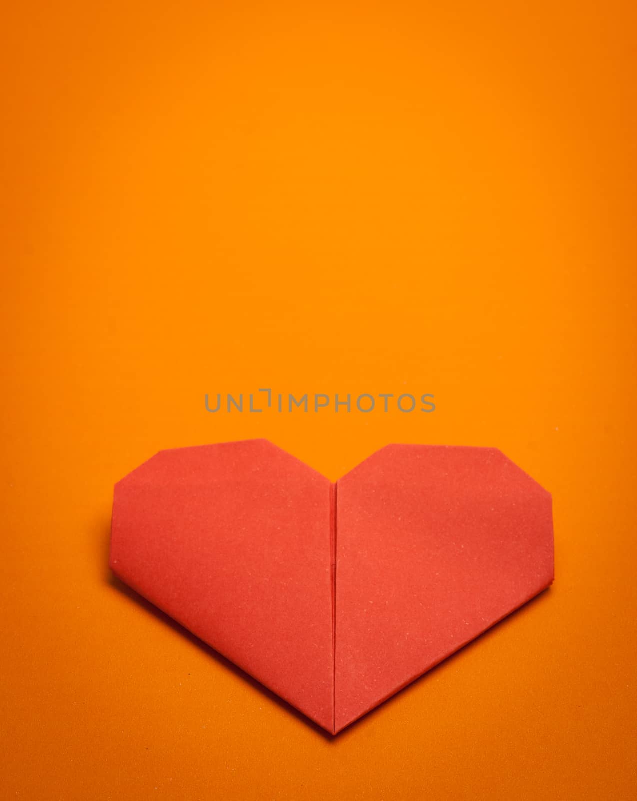red origami paper heart on orange paper background