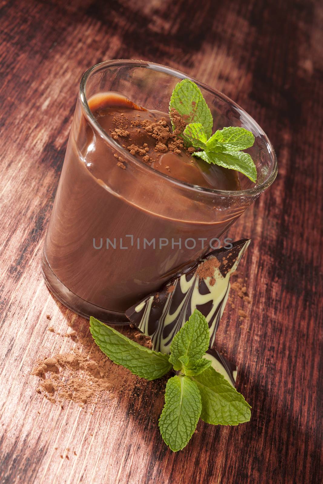 Delicious chocolate pudding with cocoa powder, chocolate bar and fresh mint on wooden background. Culinary sweet dessert. 