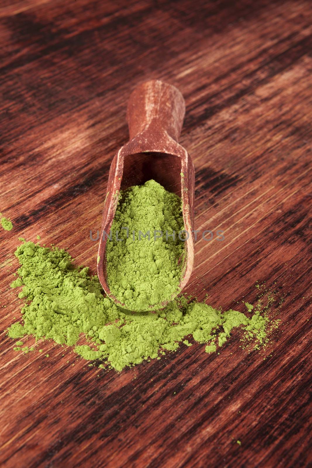 Green food supplement. Wheatgrass ground on brown wooden scoop on brown wooden background. Healthy natural detox. 