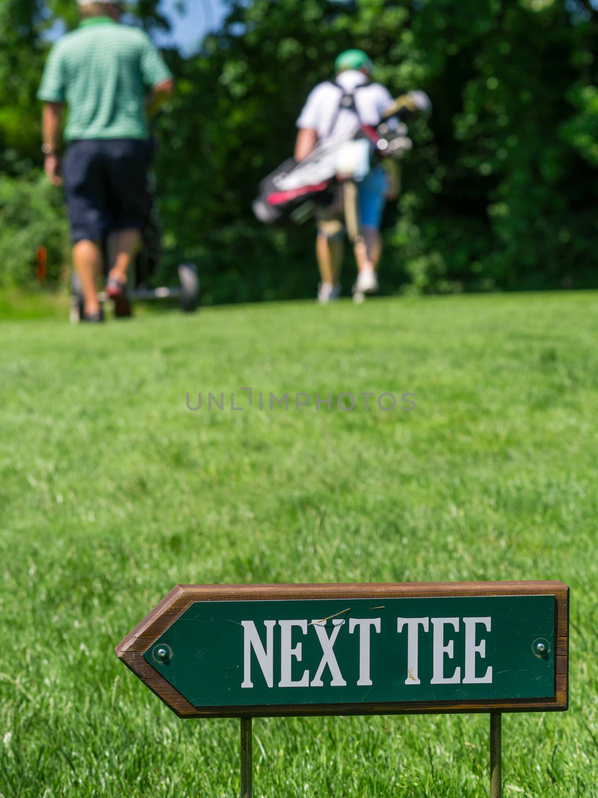 Photo of a Next Tee sign at a golf course with two blurry golfers walking behind.