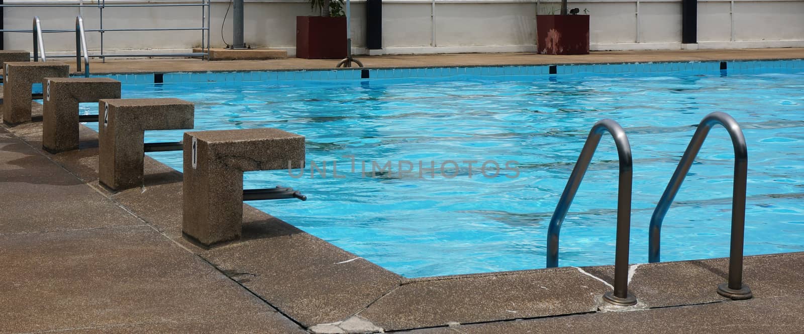 Public pool with clear blue water, stand for jump and see a ladder for access to the swimming pool.                               