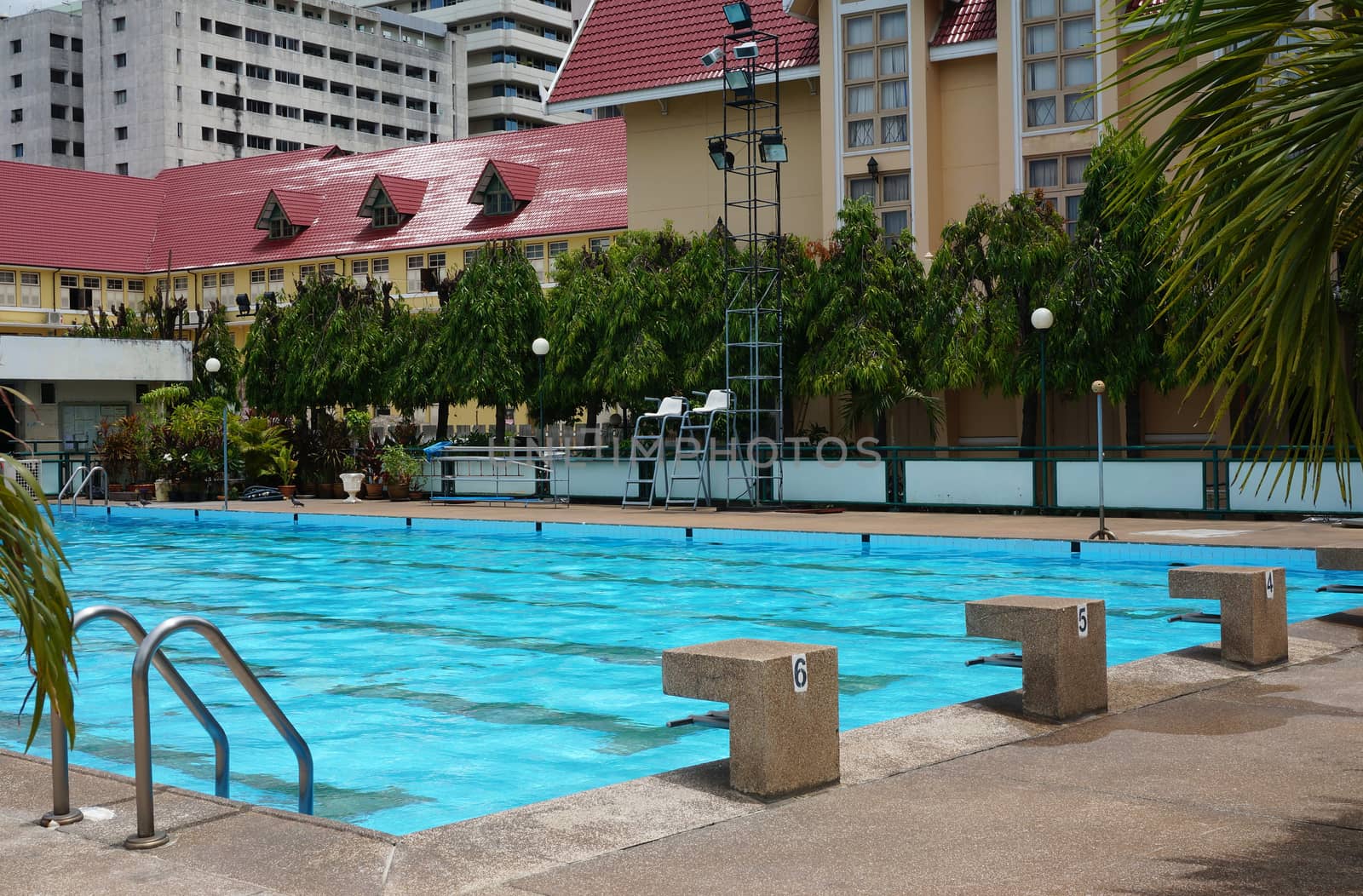 Public pool with clear blue water, stand for jump and see a ladder for access to the swimming pool.                               