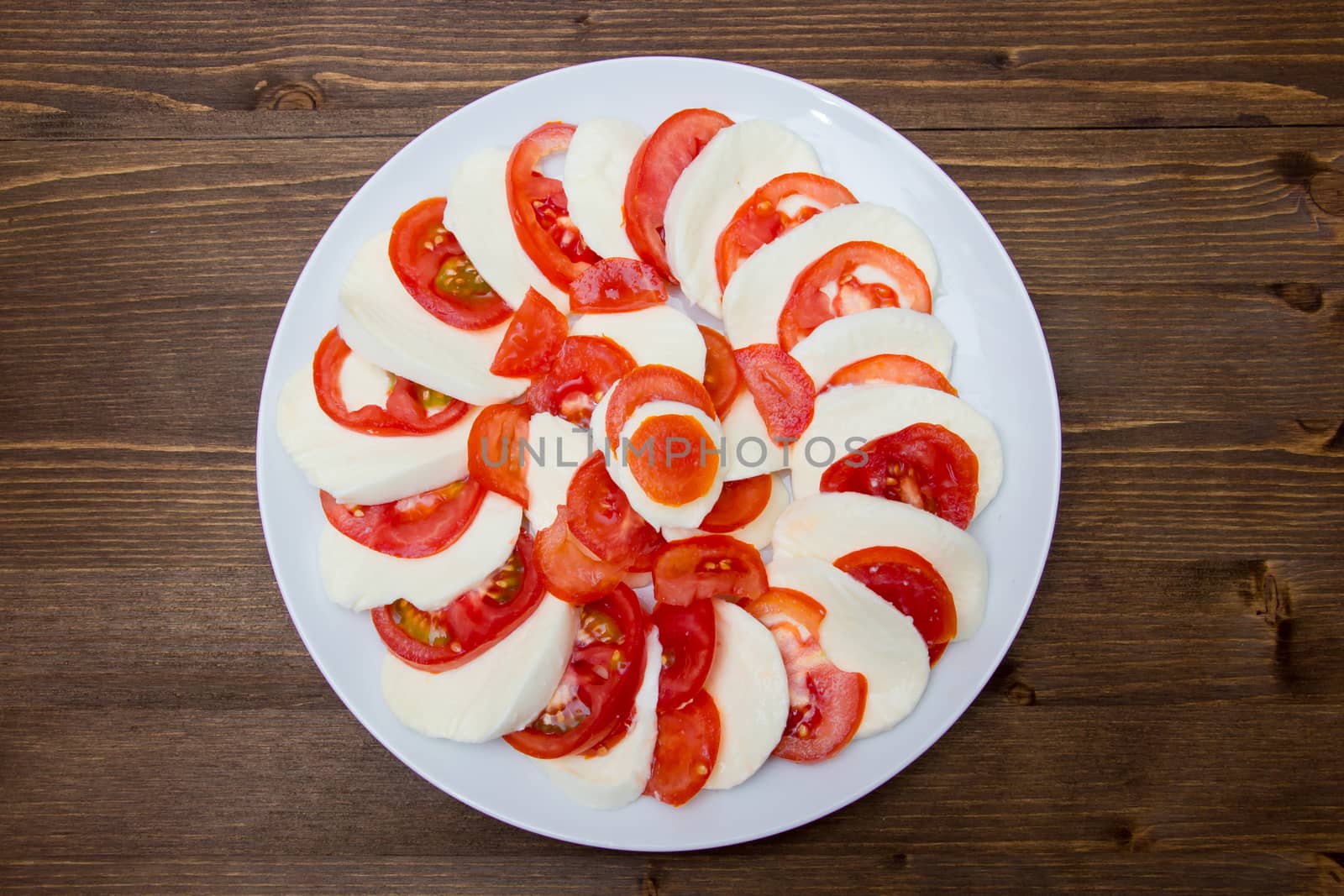 Tomato and mozzarella on a plate on a wooden table seen from above