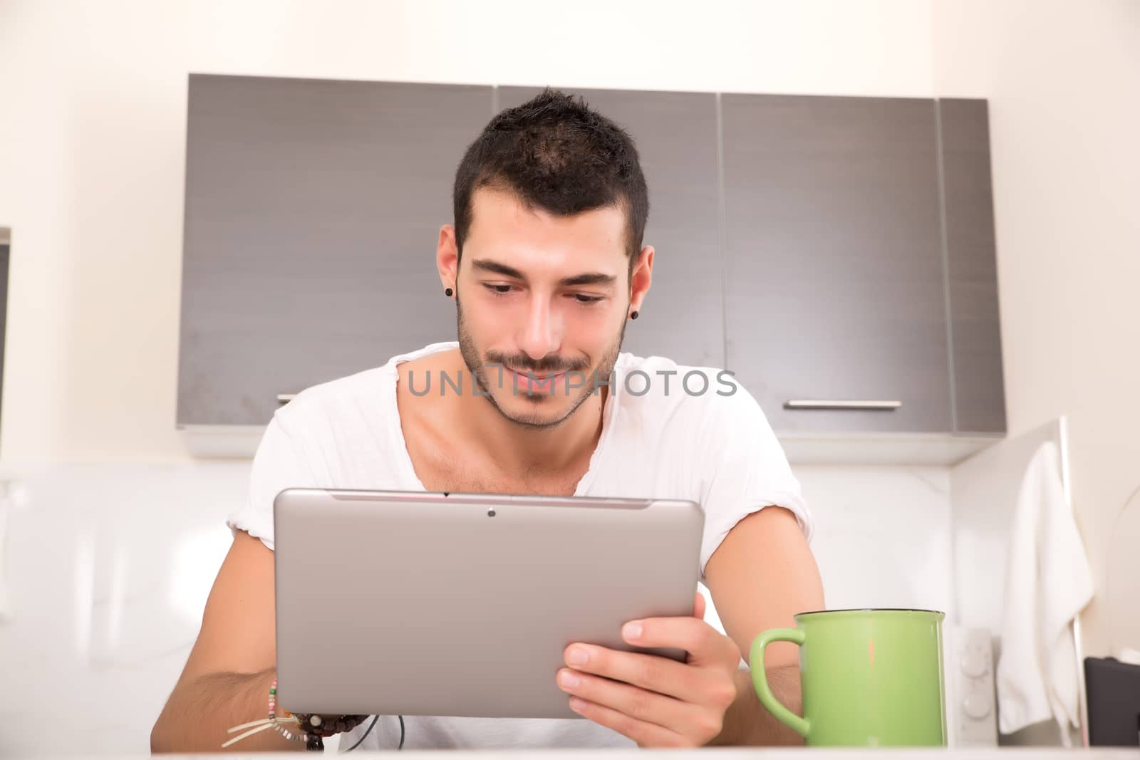 A young male sitting in the kitchen with a Tablet PC.