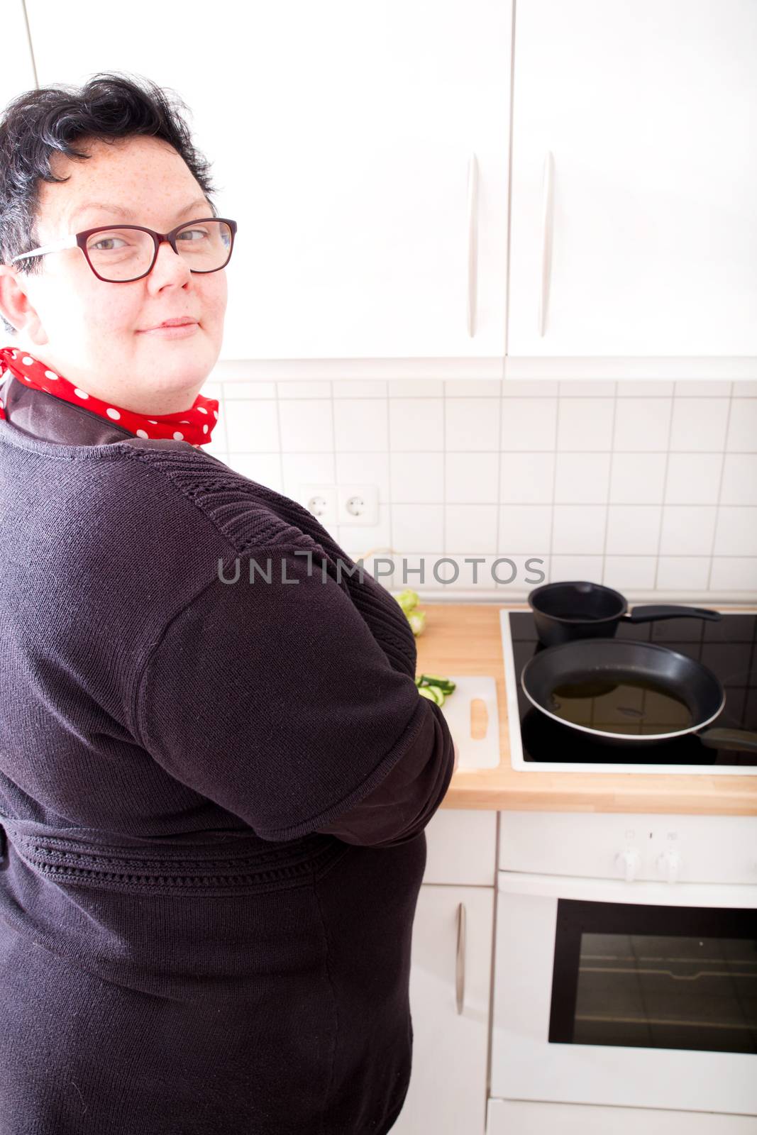 Mature overweight woman cutting cucumber in the kitchen.
