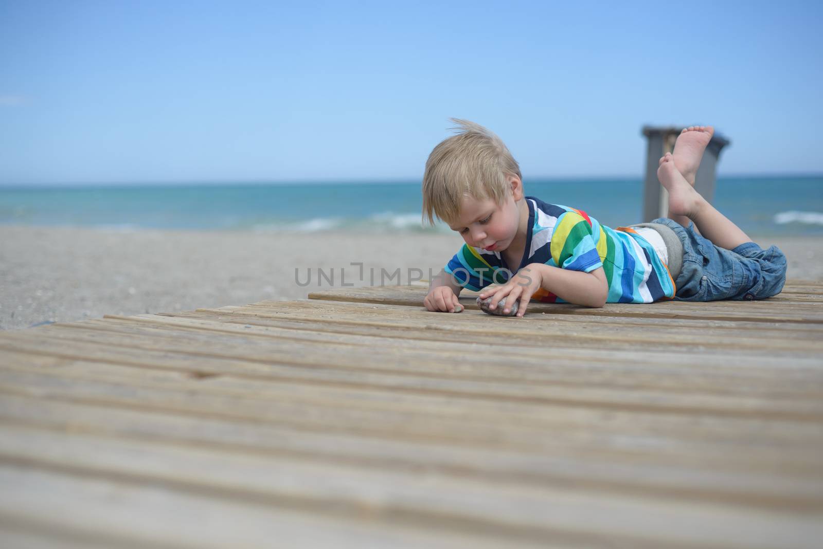 Small boy resting on a wooden walkway on the beach