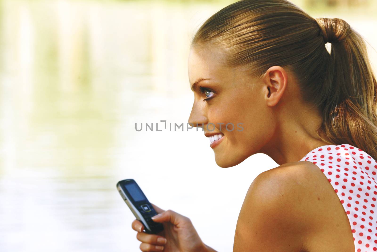 Young blond woman with mobile phone in the park 