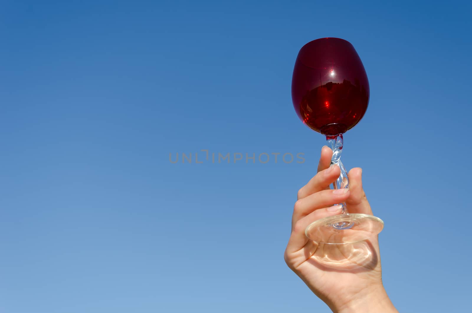 hand hold red wineglass squirm stem on blue sky by sauletas