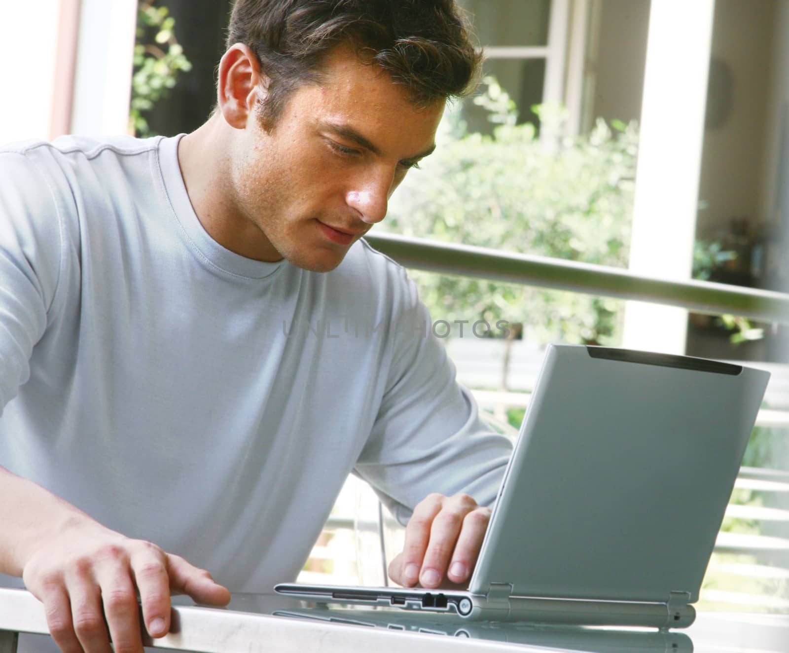 young man in t-shirt sitting on sofa at home, working on laptop computer
