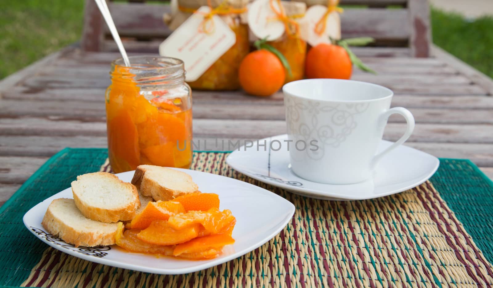 Homemade tangerine marmalade, two slices of bread on the white square plate and a cup of milk.