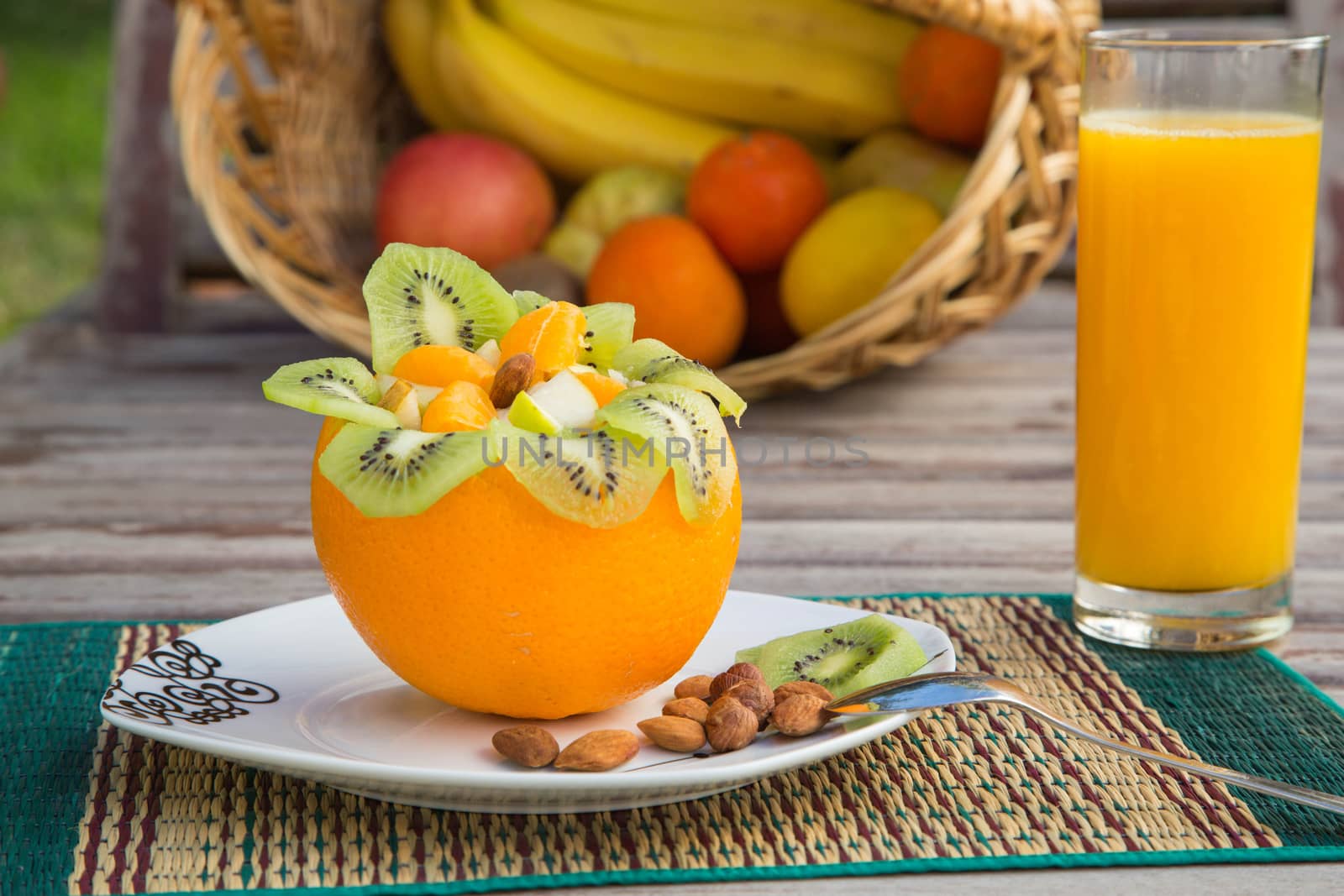 Fruit salad in the orange skin and a glass of fresh orange juice. A basket with exotic fruits in the background