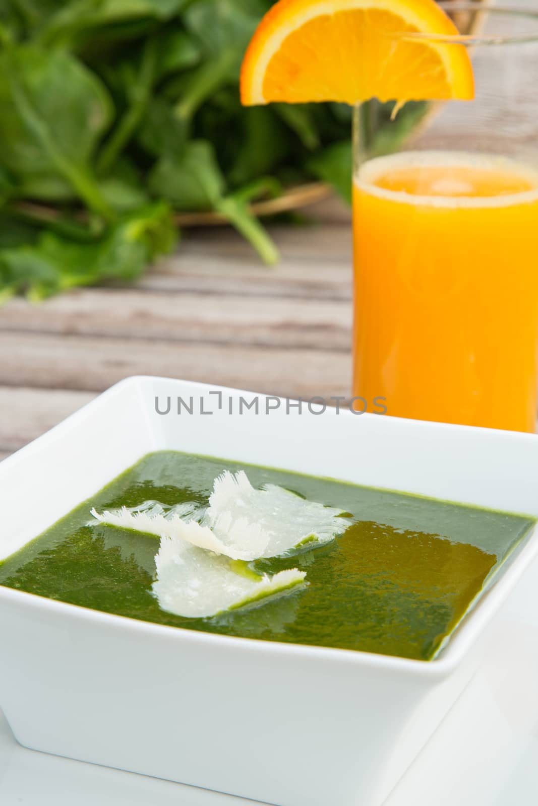 Spinach cream soup in the white square plate and a glass of fresh orange juice. Fresh leaves of spinach in the background