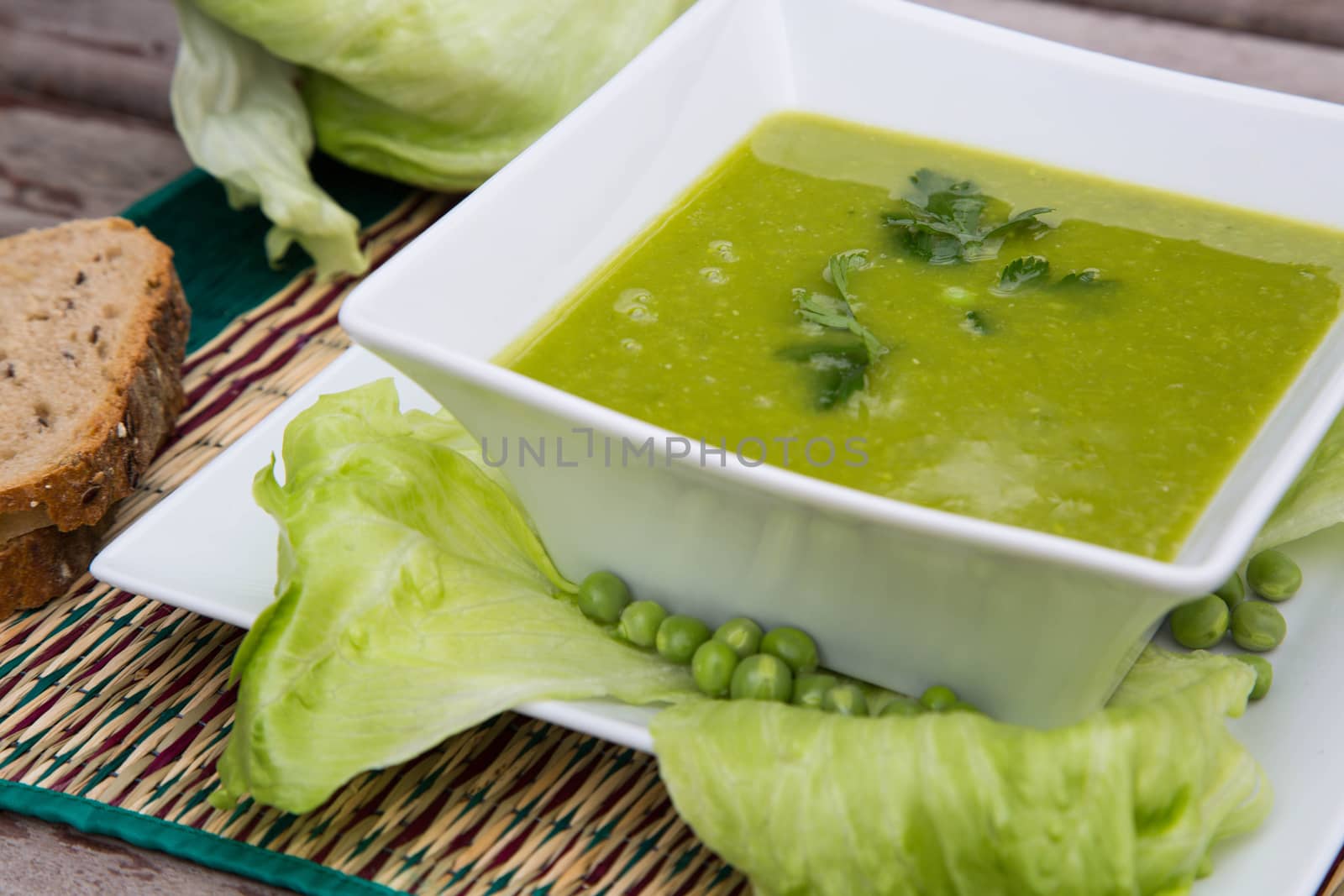 Green peas cream soup with salad leaves and fresh parsley in the white square plate