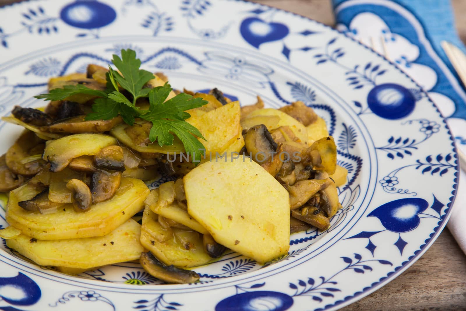 Baked potatoes with mushrooms and parsley on the white blue plate.