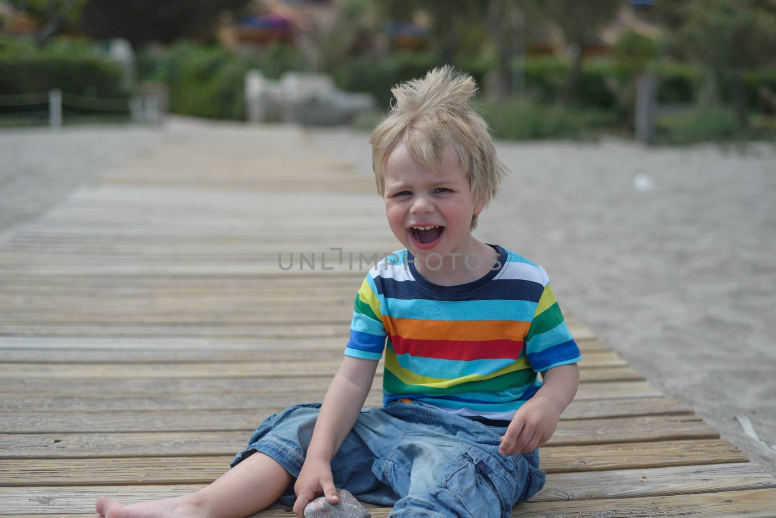 Flashy small boy sits on a wooden walkway on the beach