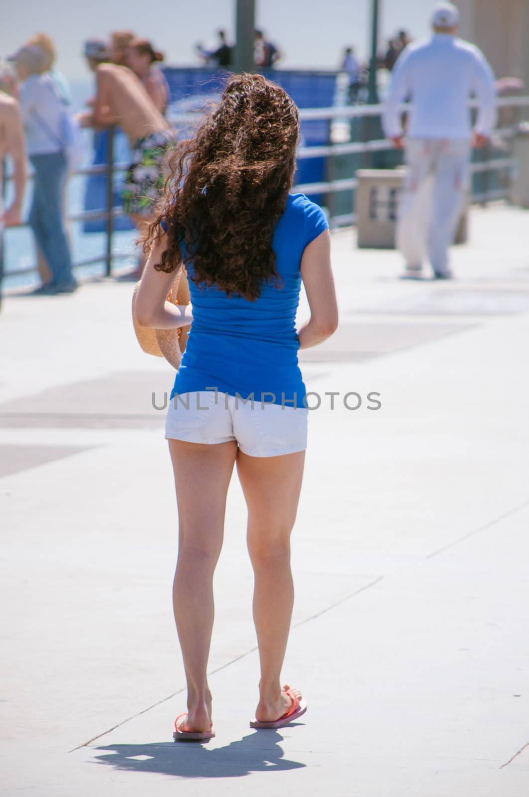 Beatiful female model wearing white shorts and blue shirt on beach pier walking.