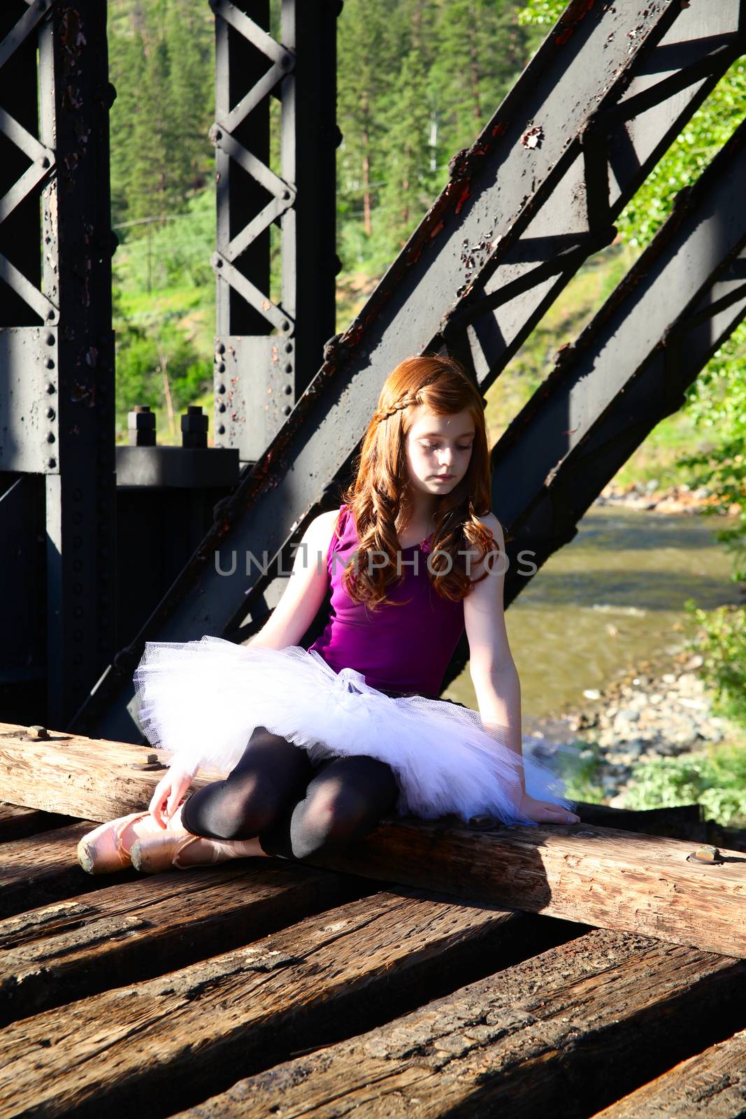 Beautiful girl wearing a white tutu sitting on a bridge 