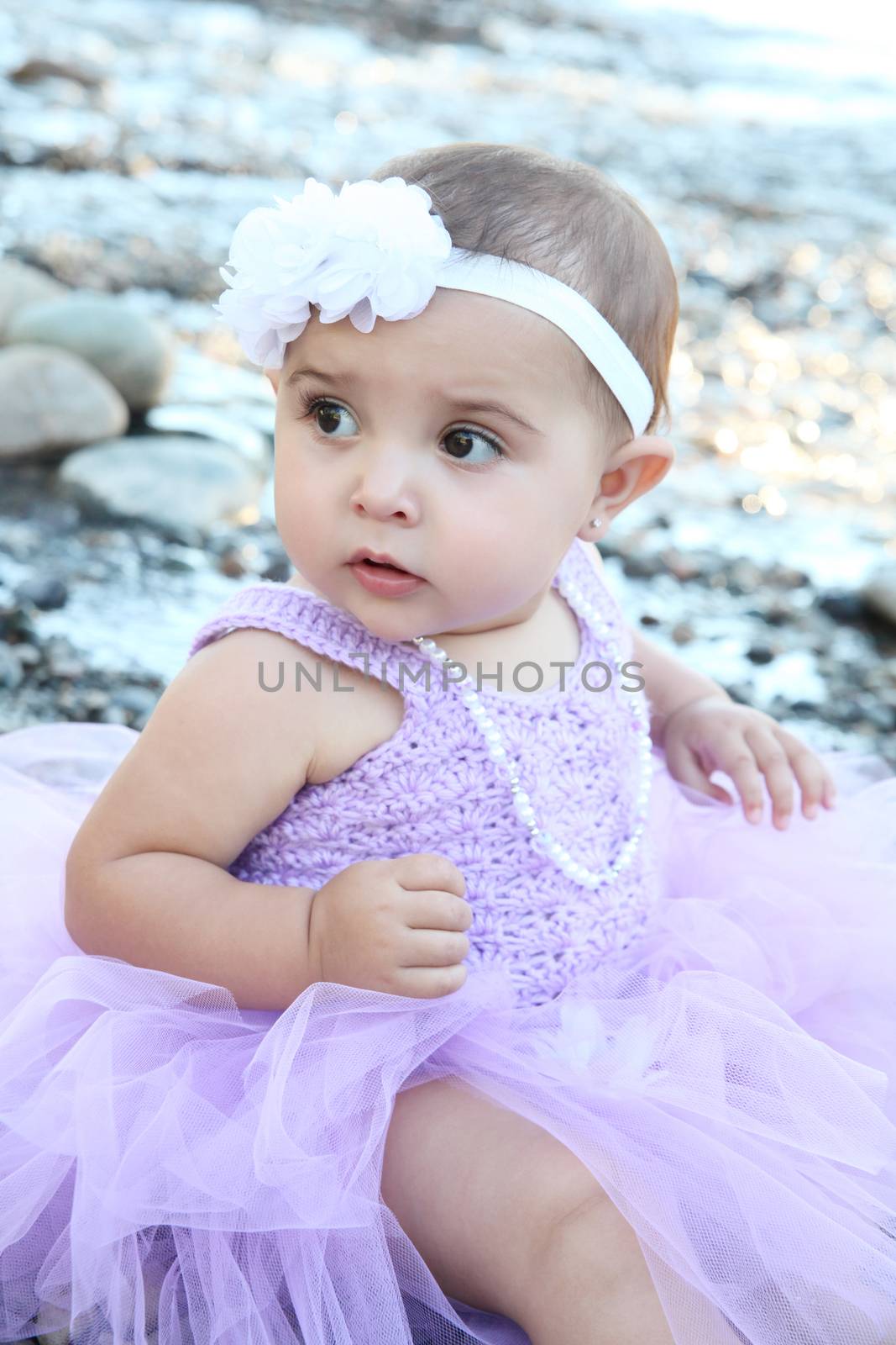 Beautiful brunette baby girl sitting on pebble beach