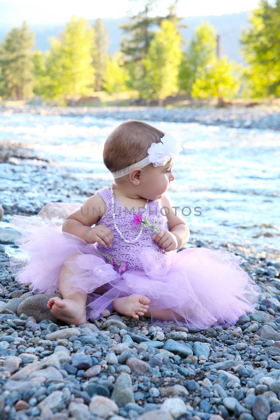 Beautiful brunette baby girl sitting on pebble beach