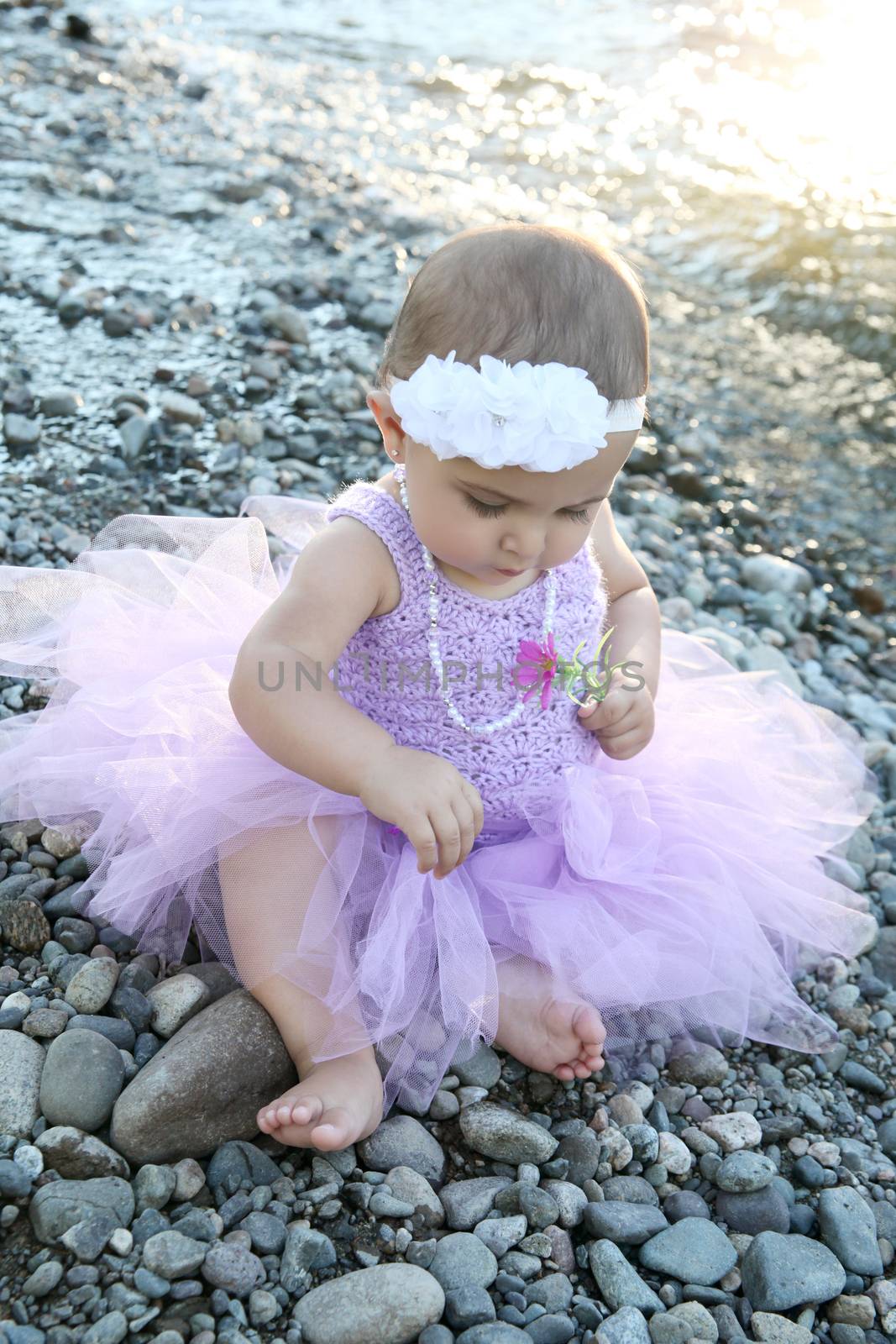 Beautiful brunette baby girl sitting on pebble beach