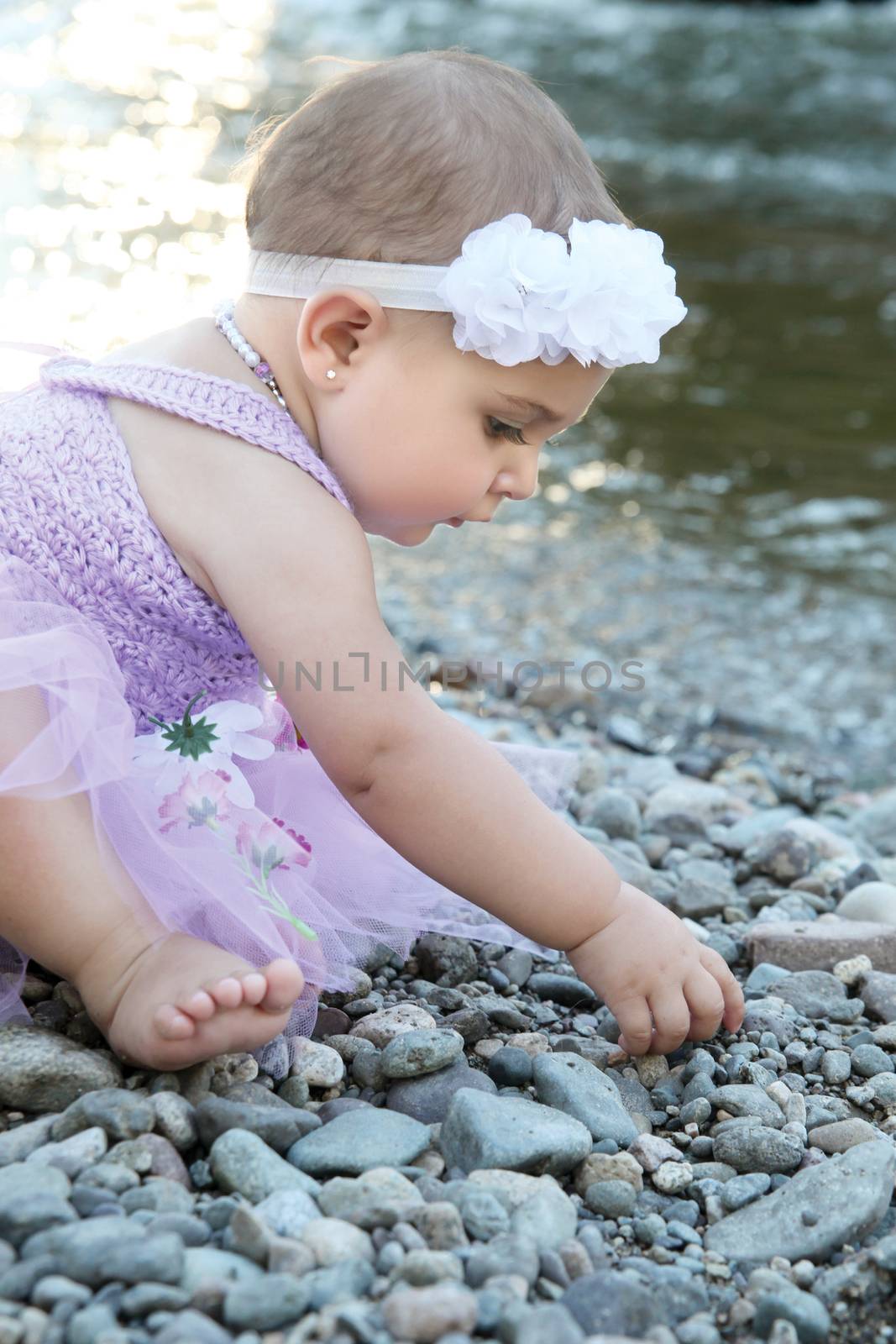 Beautiful brunette baby girl sitting on pebble beach