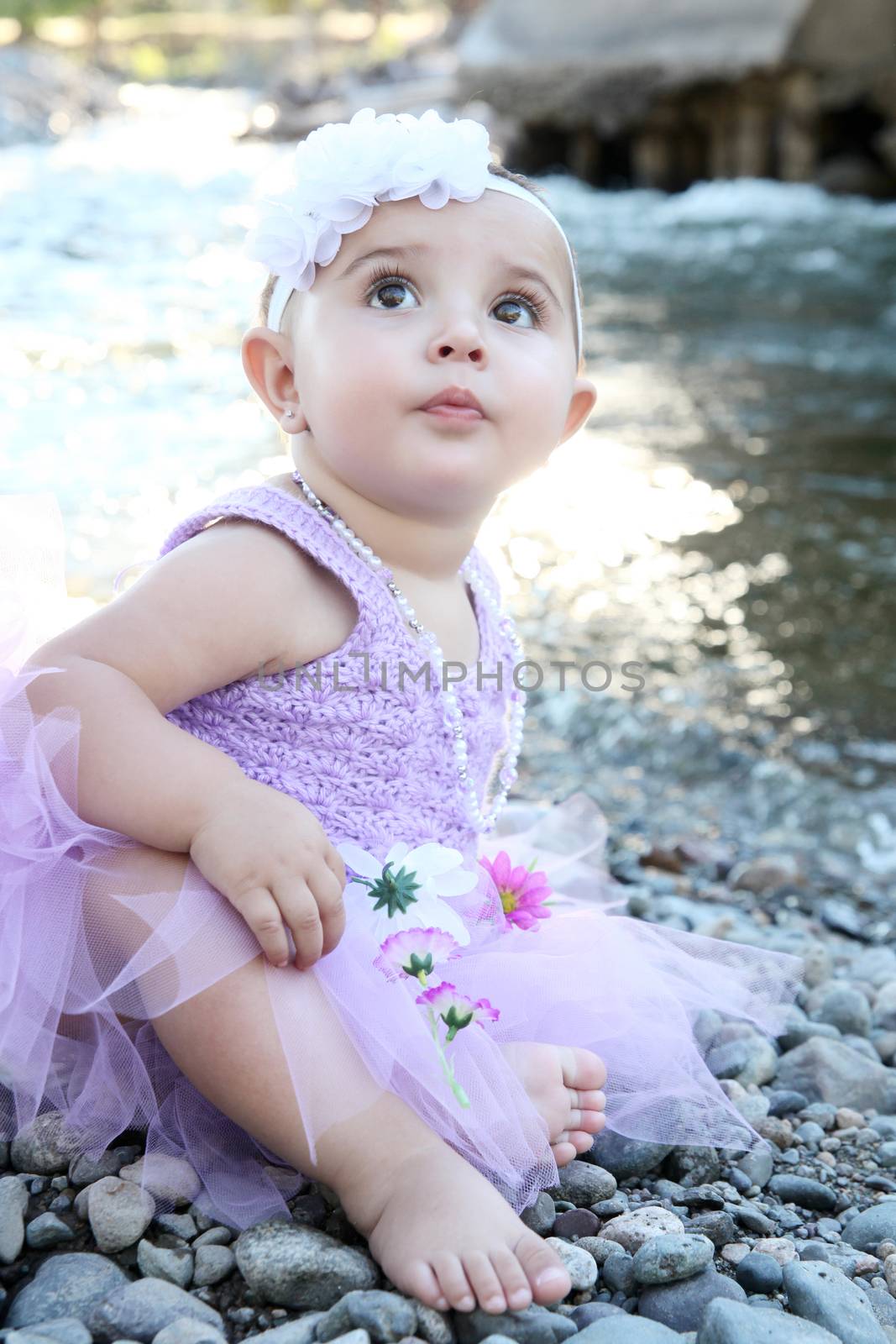 Beautiful brunette baby girl sitting on pebble beach