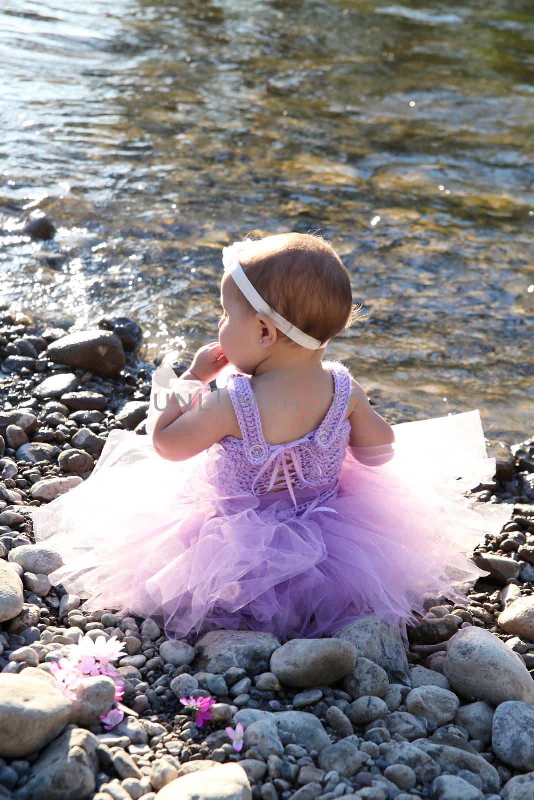 Beautiful brunette baby girl sitting on pebble beach