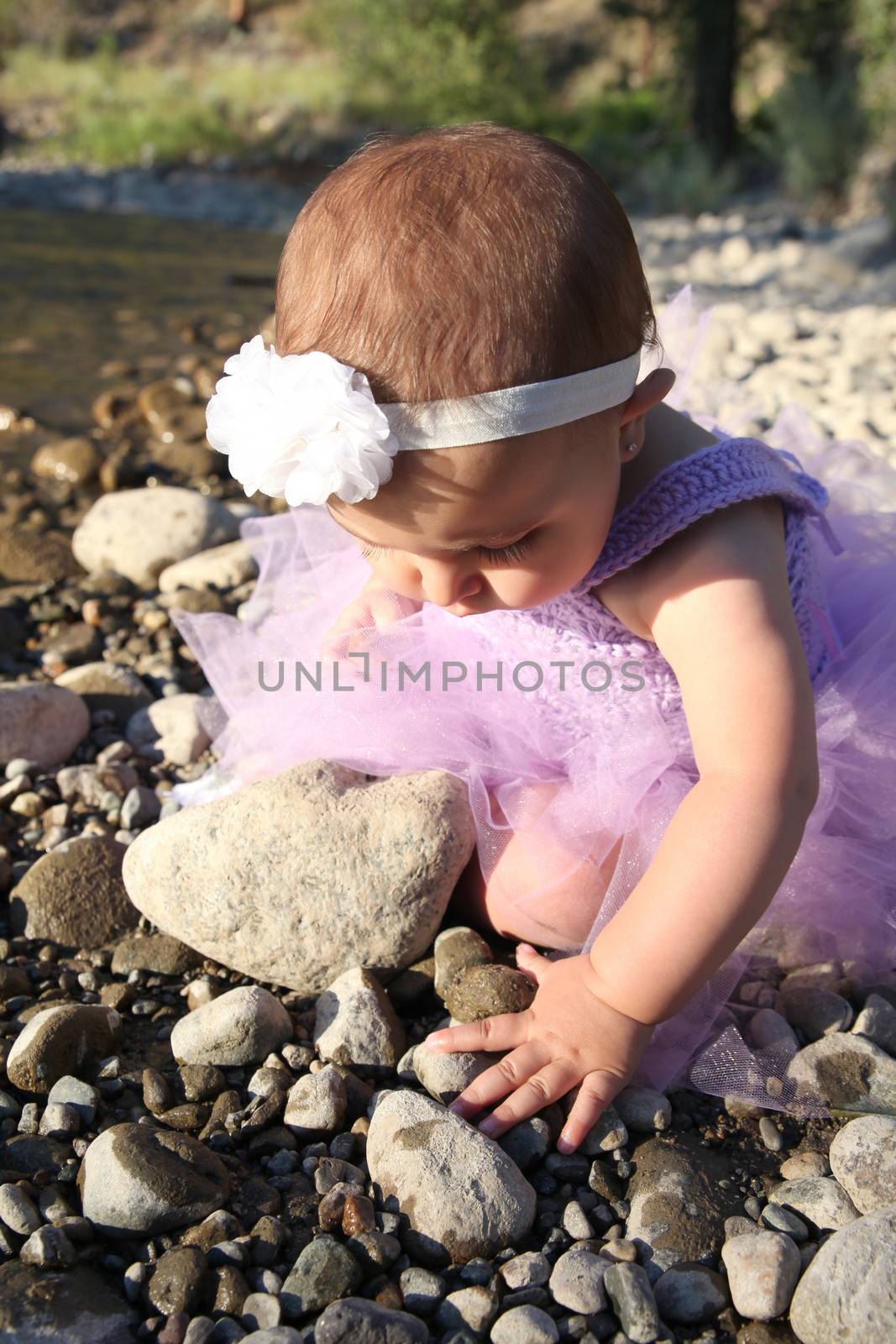 Beautiful brunette baby girl sitting on pebble beach