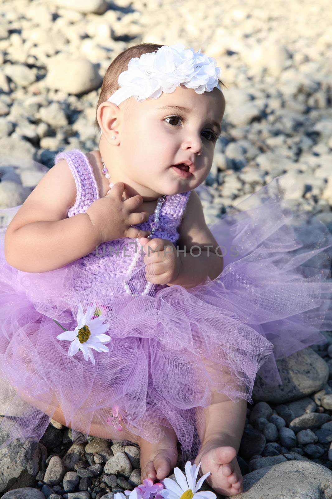 Beautiful brunette baby girl sitting on pebble beach