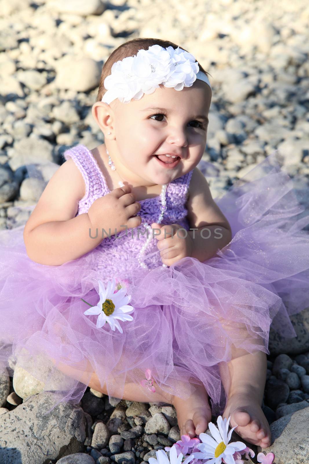 Beautiful brunette baby girl sitting on pebble beach