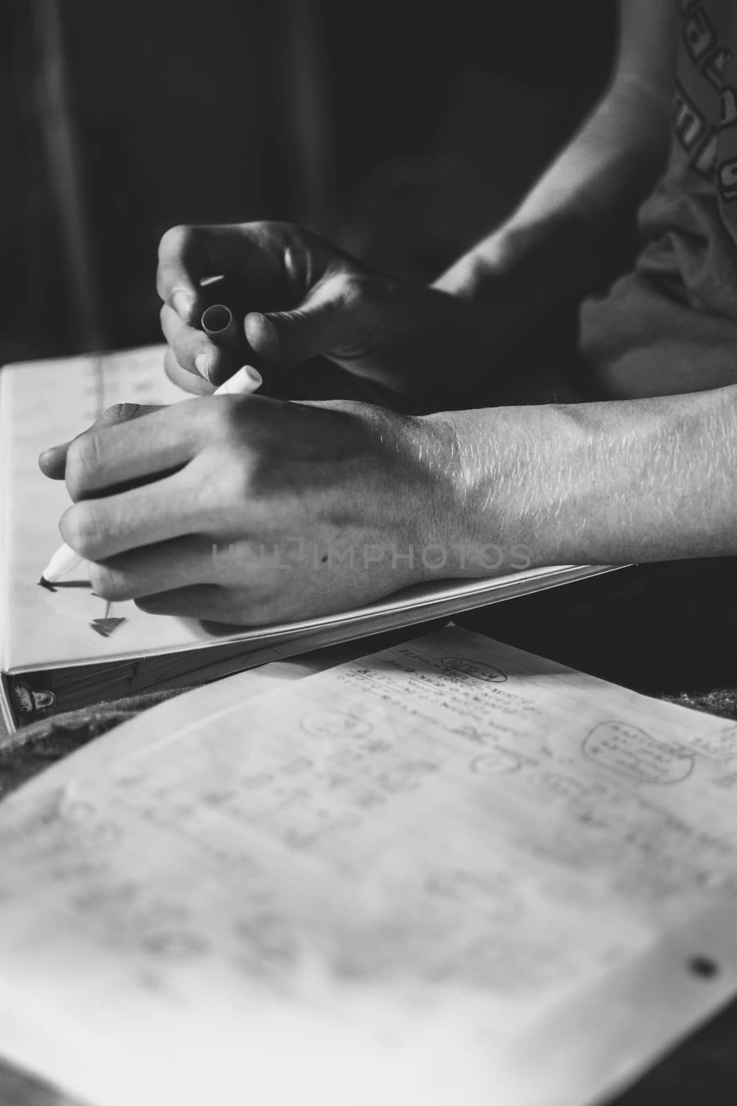 Black and white close-up of the hands of a teenage student doing his homework assignment, consisting of solving a mathematical exercise or problem, with intellectual effort, by writing, on paper