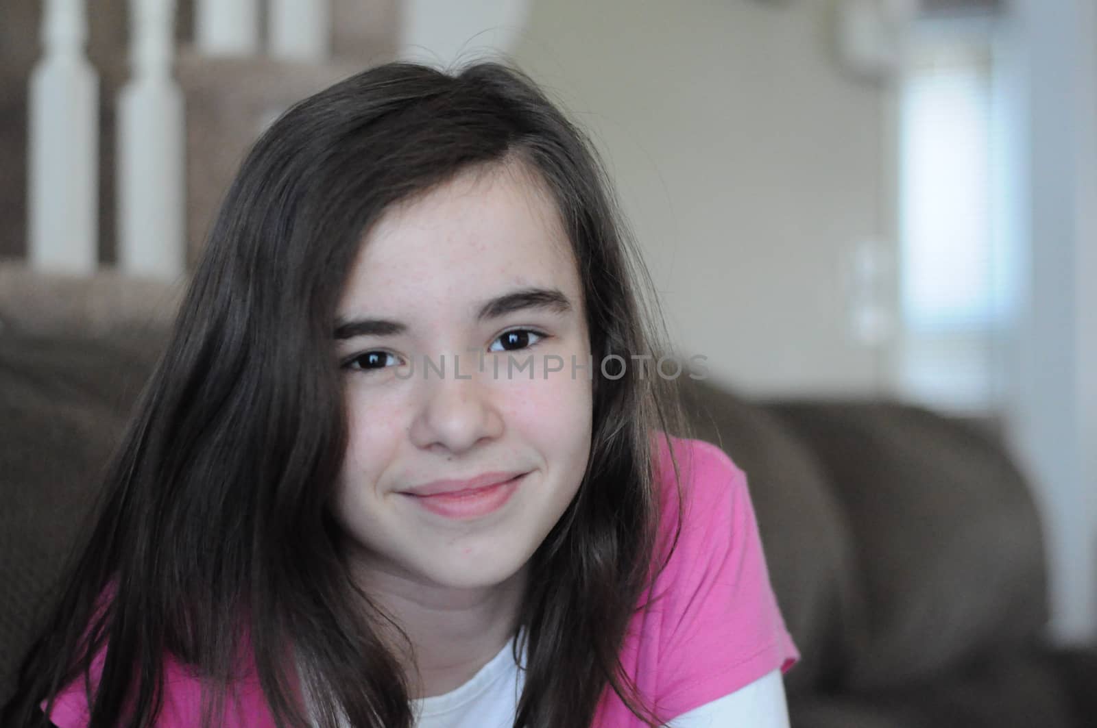Portrait of a brunette long-haired pretty teenage girl smiling at camera with a happy and confident facial expression, wearing a pink T-shirt, indoors
