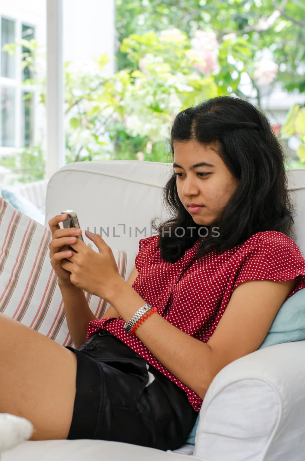 Young woman with her smart phone sitting on sofa in living room 