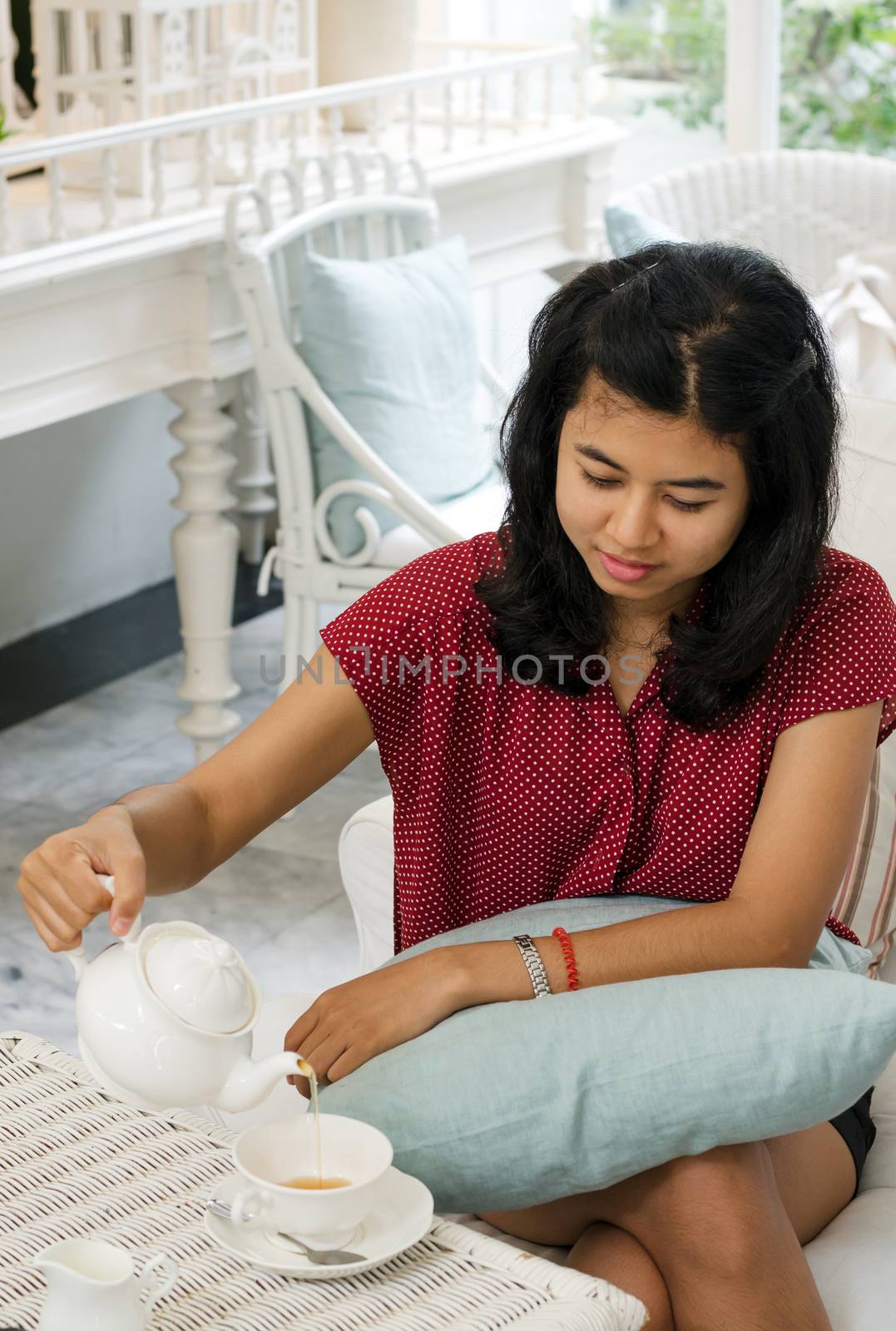 Woman pouring tea from the teapot into a white ceramic cup at vintage cafe