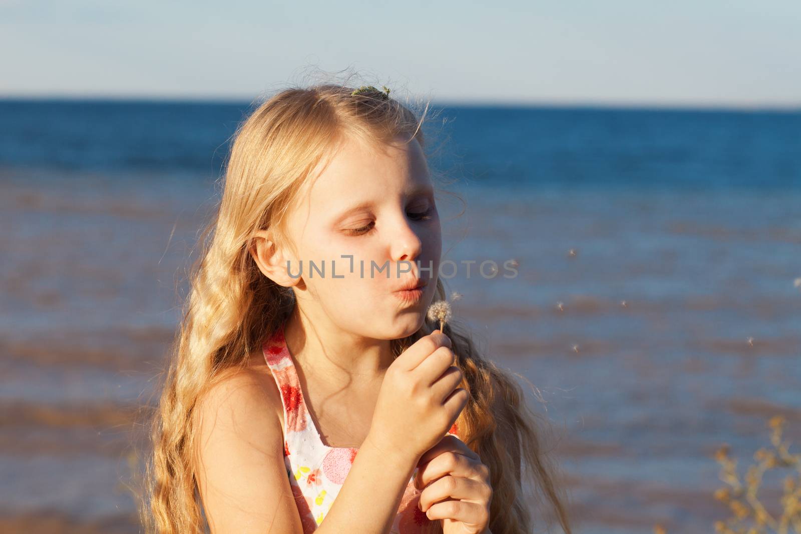 gilrl blowing on dandelion on the seashore