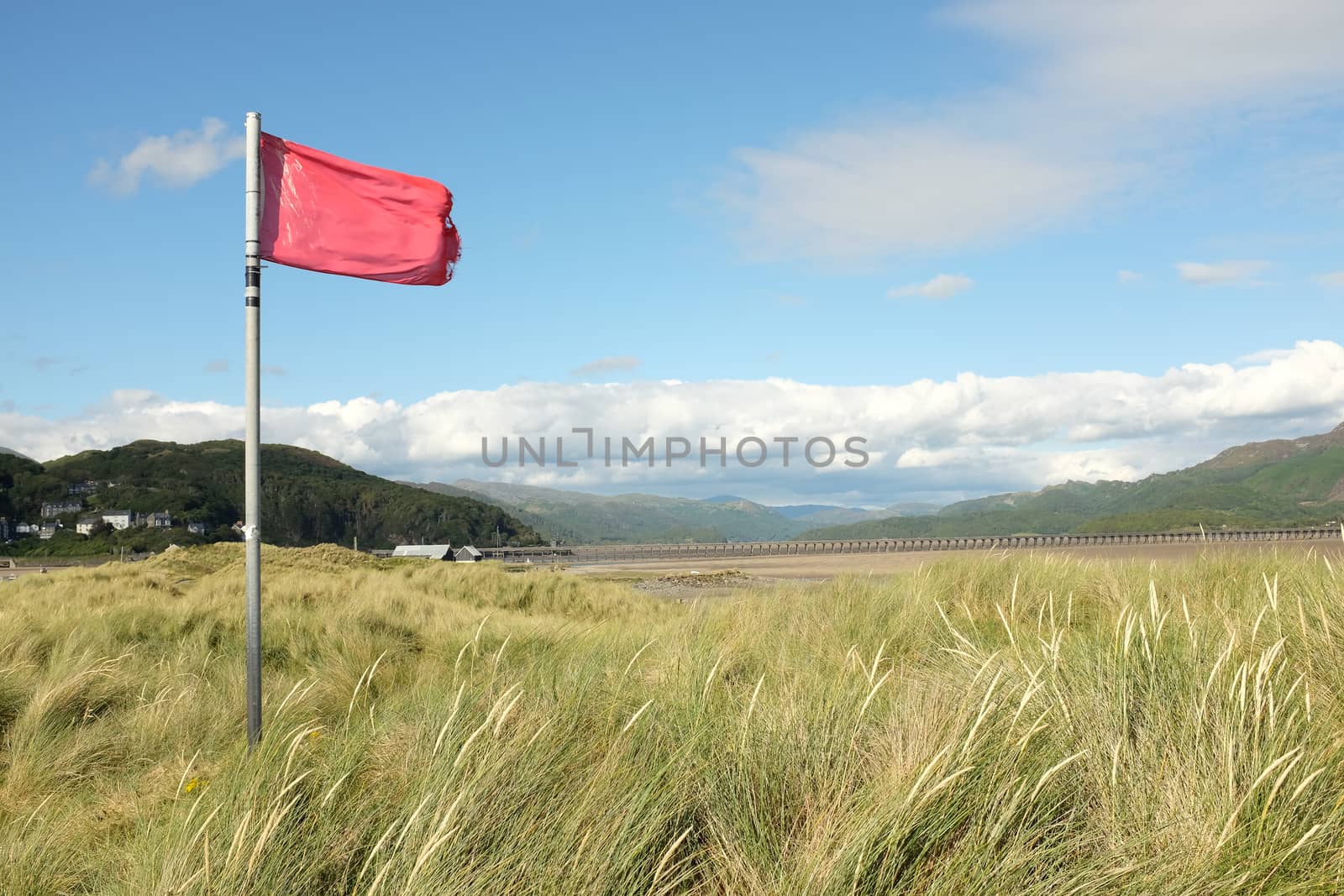 A red warning flag on a post on a sand dune over looking an estuary.