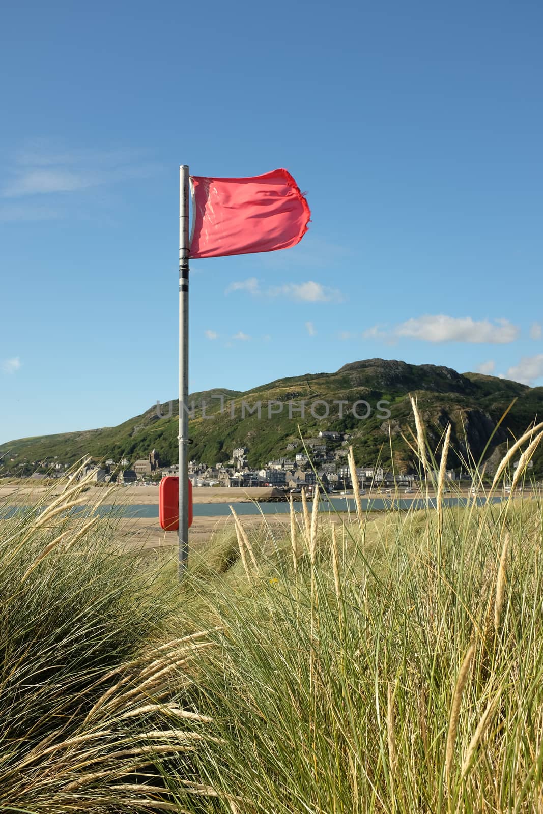 A red flag flutters in the wind over looking an estuary with a town in the distance.