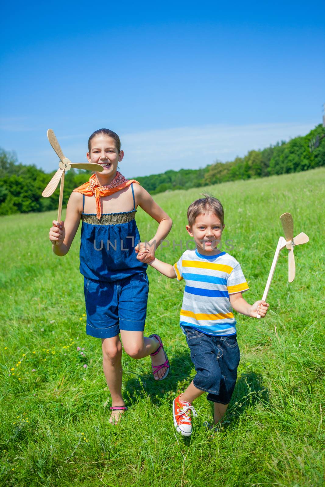 Cute kids runing on grass in summer day holds wooden windmill in hand