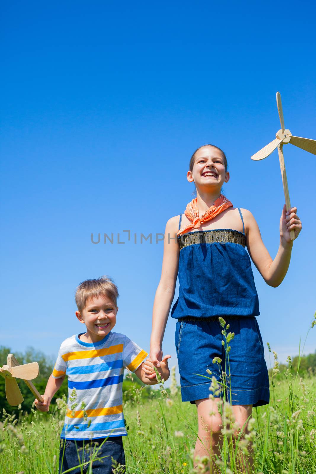 Cute kids runing on grass in summer day holds wooden windmill in hand