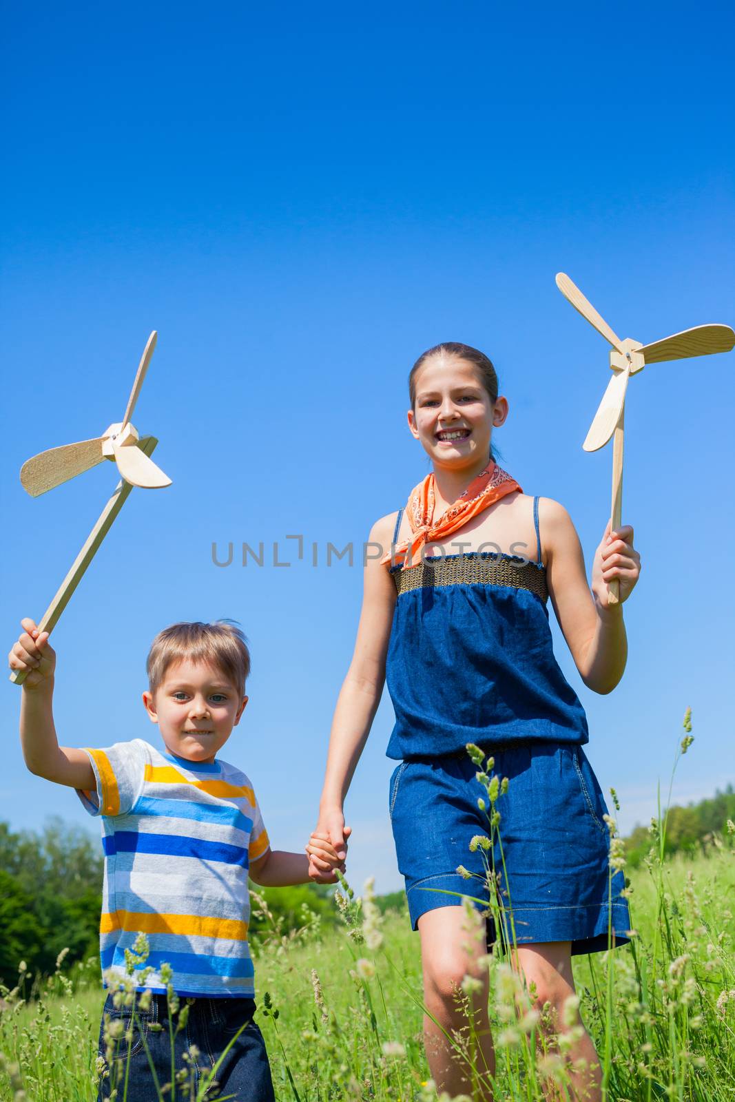 Cute kids runing on grass in summer day holds wooden windmill in hand