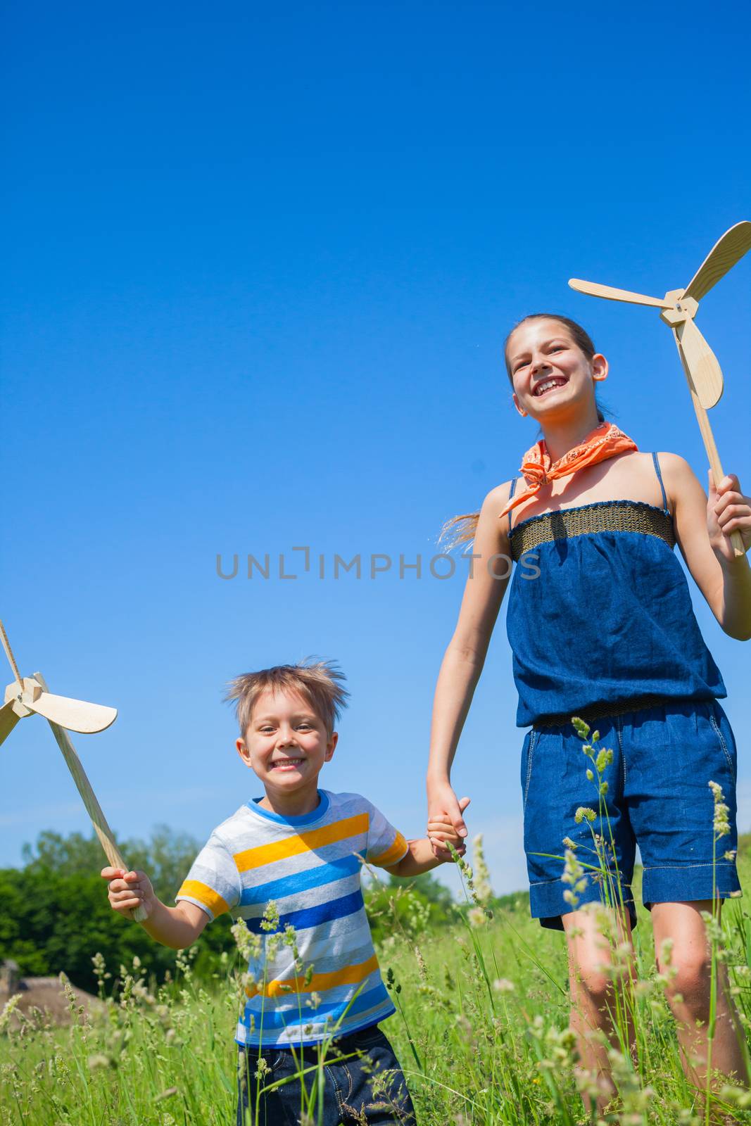 Cute kids runing on grass in summer day holds wooden windmill in hand