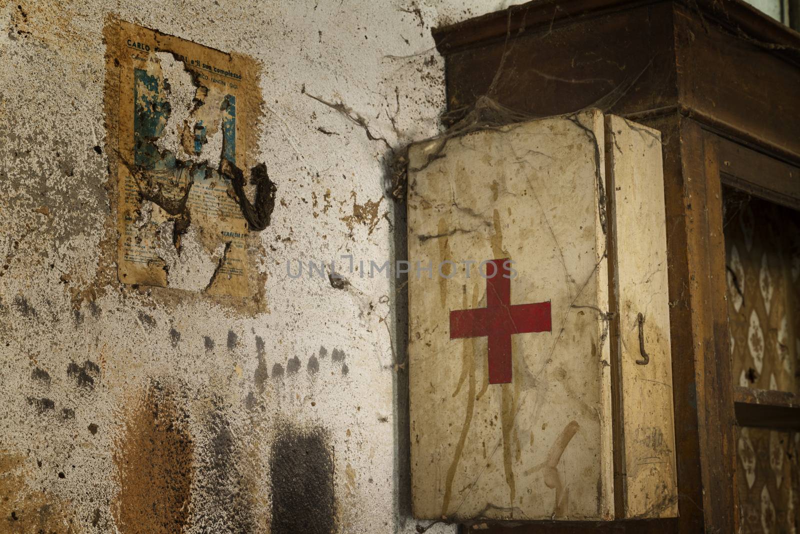 An old first aid kit on a dirty and rusty wall covered by cobwebs