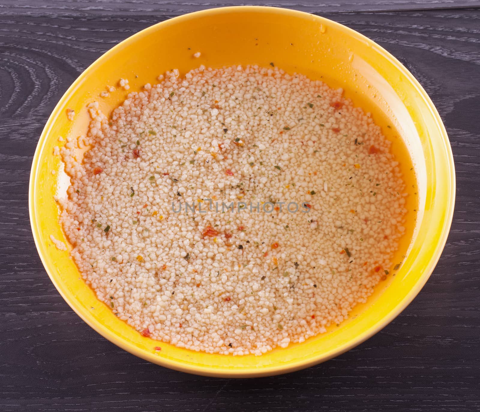 Cous cous in a yellow plate, over wooden table