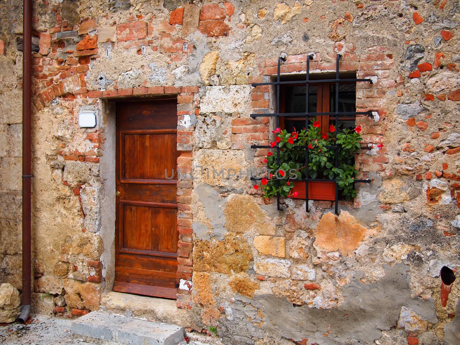 Old wooden door in a brick facade with flowers of a house in an old Italian town.