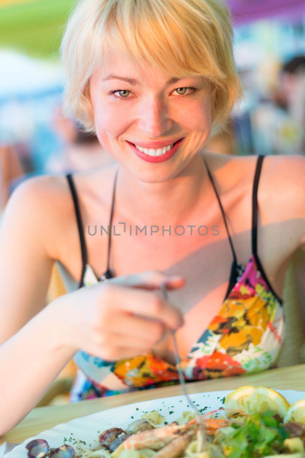 Closeup of a cheerful young woman eating healthy mediterranean sea food meal on the outdoor restaurant terrace.
