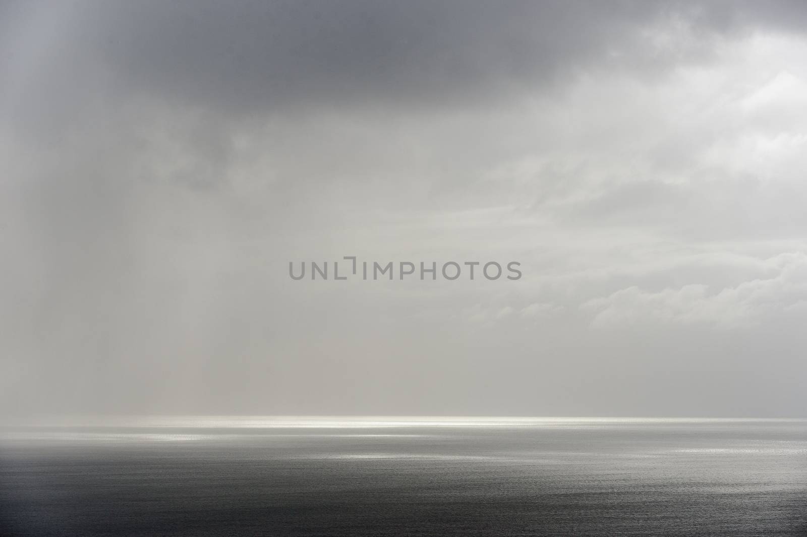 Calm seascape with stormy sky where sun-rays get through the clouds. 