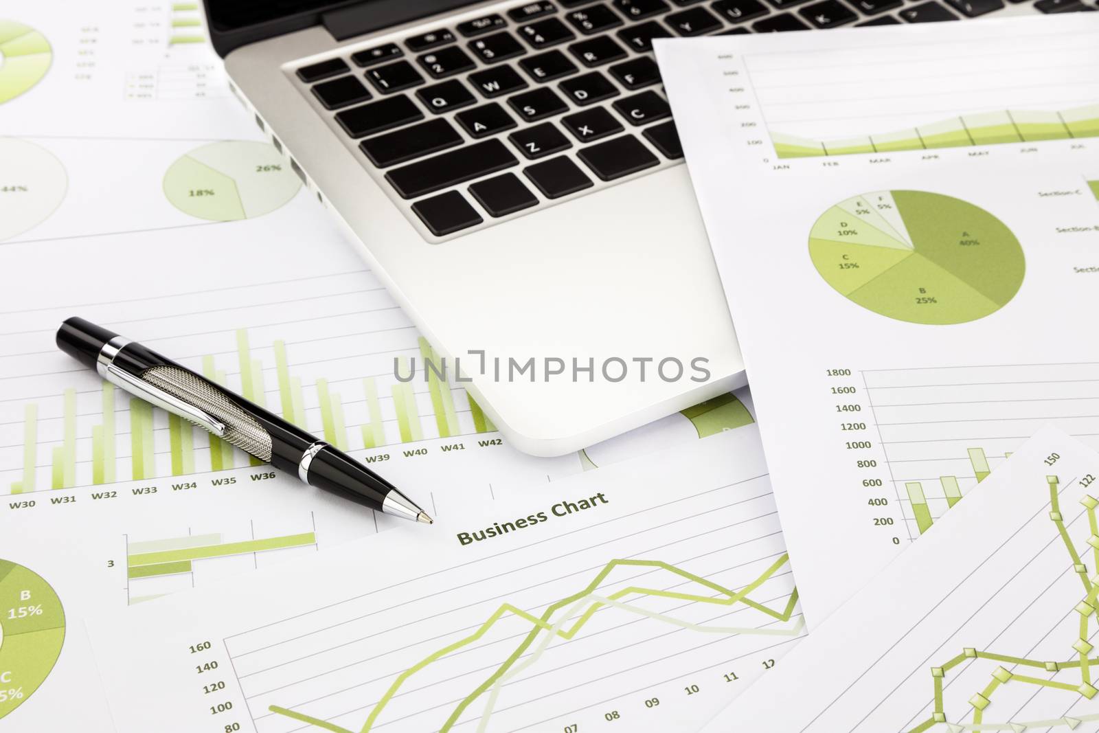 laptop and pen with green business charts, graphs, information and reports background for financial and business concepts
