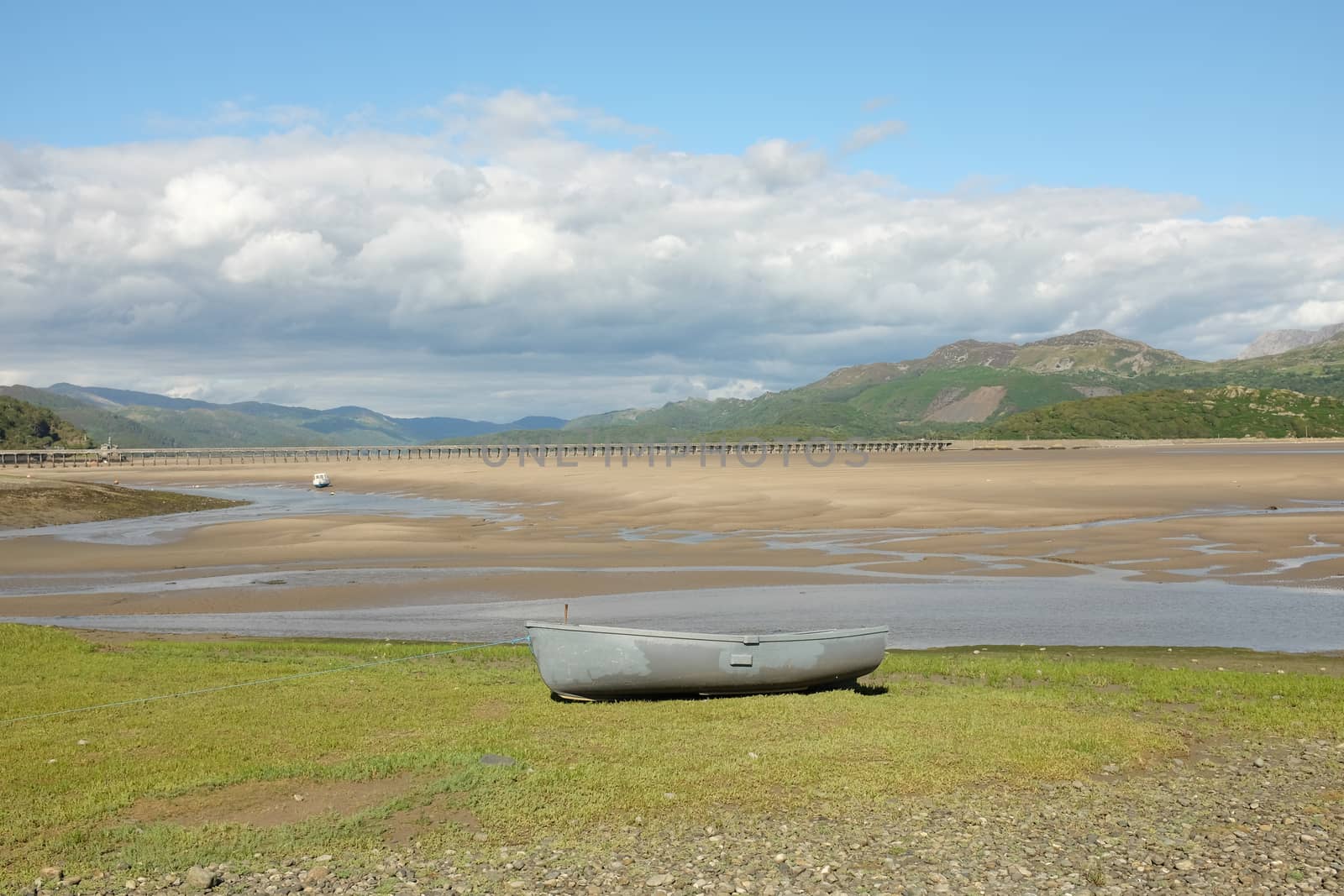 A grey painted boat on the bank overlooking an estuary with the tide out.