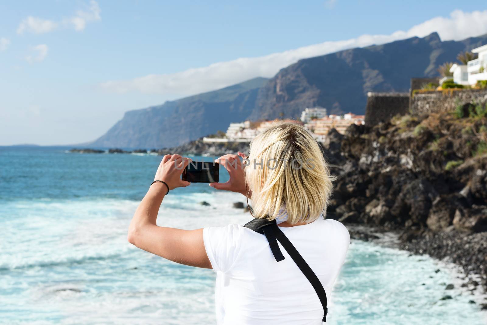 Young blond woman taking pictures of Tenerife coast by Nanisimova